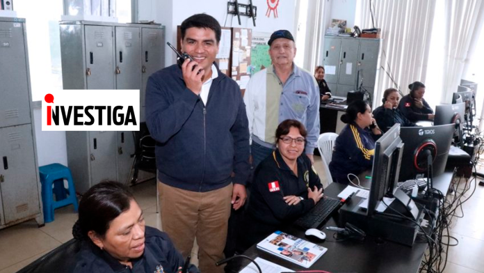 Team of investigators in a busy control room with desks, monitors, and radios; man in front uses a handheld radio, logo reads 'INVESTIGA' on the wall.