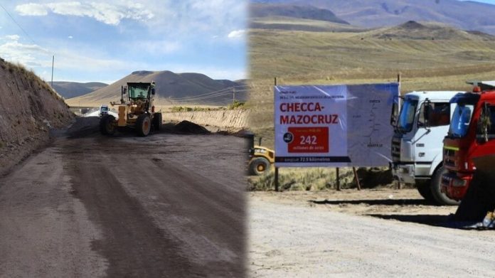 Construction site on a dirt road with a bulldozer in the foreground and trucks beside a banner in a rural valley.