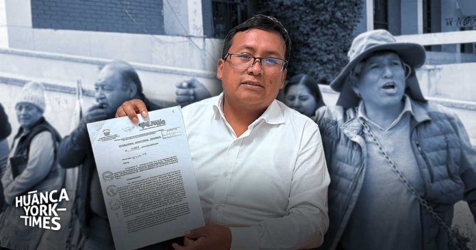 Man in white shirt holds a document, facing the camera, with a group of people blurred in the background; Huanca York Times logo visible in the corner.