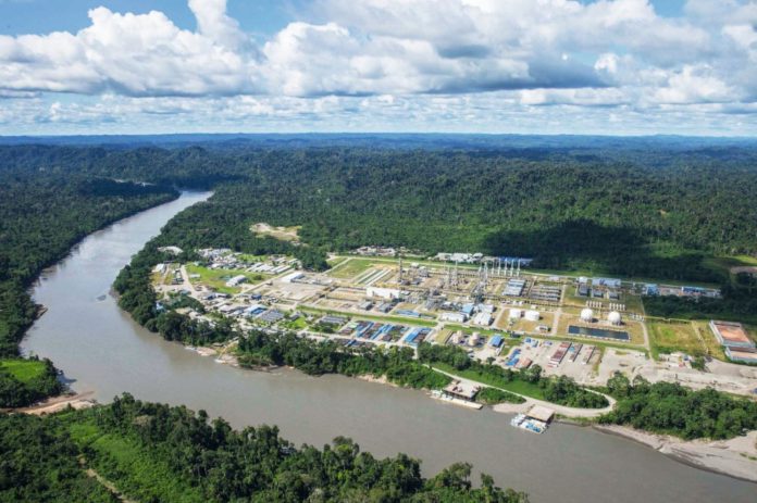 Aerial view of an industrial complex along a wide winding river, bordered by dense tropical forest.