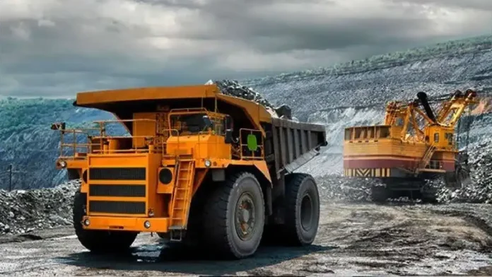 Large orange mining dump truck with heavy tires in a rocky quarry, an excavator visible in the background.