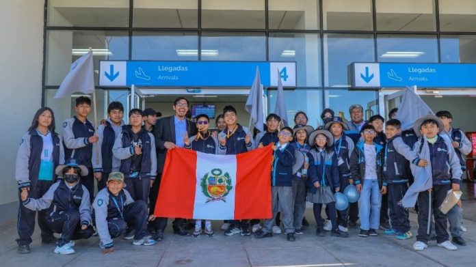 Group of students posing with a Peru flag at an airport arrivals area under blue signboards.