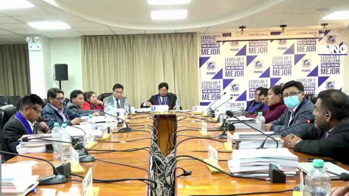 Group of officials seated around a long conference table with microphones, documents, and water bottles during a formal meeting, backdrop shows PUNO branding.