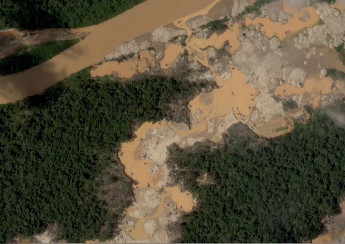 Aerial view of an orange-sediment stream washing through a rocky gorge bordered by dense green forest.