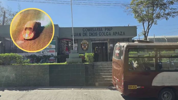 Police station building labeled 'COMISARIA PNP JUAN DE DIOS COLCA APAZA' with a brown bus parked at the curb in front. A circular inset highlights a close-up of a small object on the ground left of the image.
