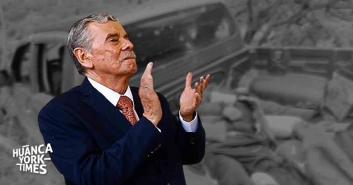 Older man in a dark suit with a red tie claps his hands, foreground colored, grayscale background with a Huanca York Times watermark.